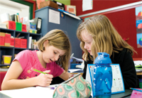 Two primary age school children in a classroom setting, working together on a written exercise