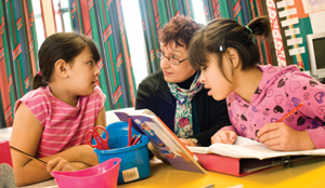 An adult educator works on a reading exercise with two primary age children 