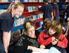 Educator sitting in chair reading to a group of intermediate-age pupils in a library setting