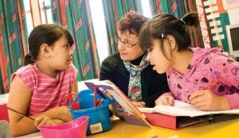 An adult educator works on a reading exercise with two primary age children 